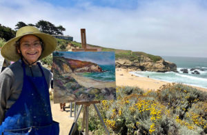 Nina Ollikainen smiles for a photo while making a “plein air” painting at Montara Beach. Ollikainen often likes to go and paint nature. “I love to be out in nature, go hiking, investigate a location and spend the day painting there,” she said. Photo courtesy of Nina Ollikainen.