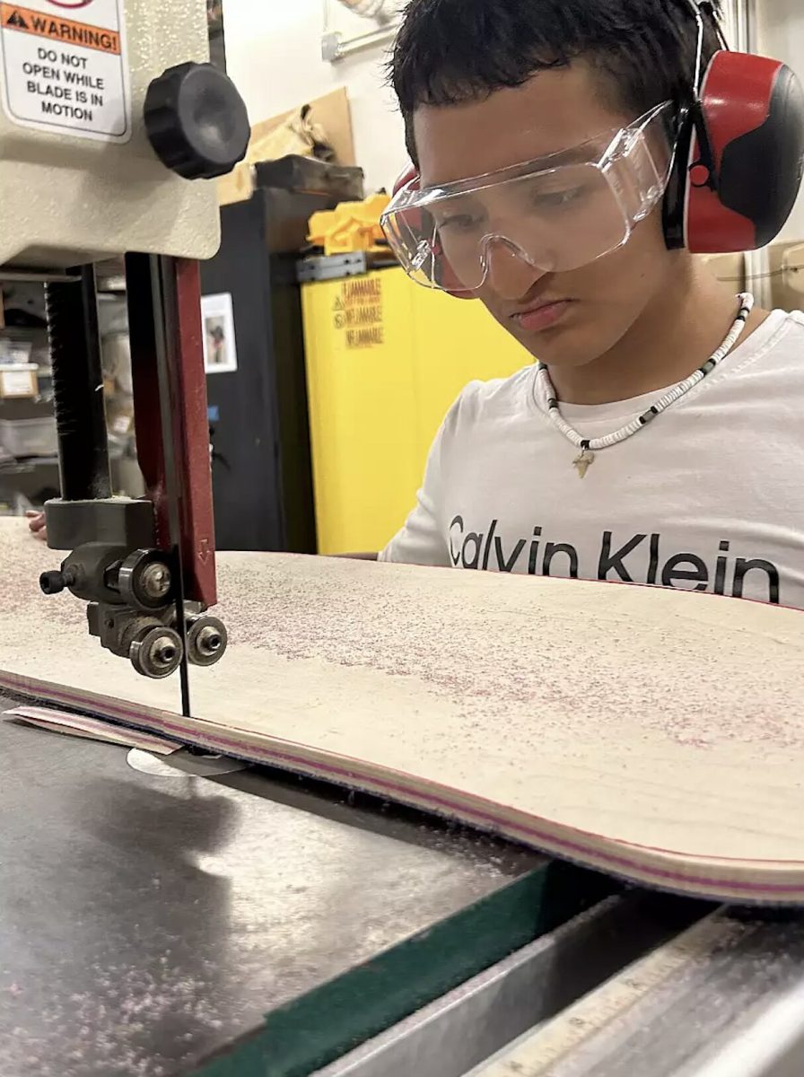 A student from Peninsula Bridge uses a bandsaw to cut out a skateboard. Photo courtesy of Jamie Formato